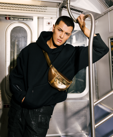 Person wearing a black hoodie and gold bag inside a subway car