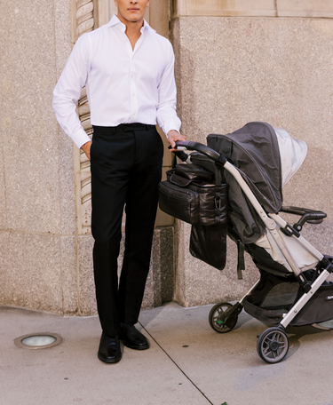 Man in white shirt and black pants holding a stroller against a stone wall.
