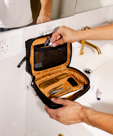 Person opening a travel-sized grooming kit on a bathroom counter.