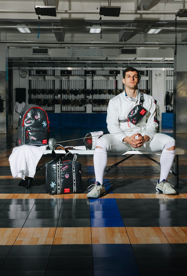 Person in fencing gear sitting on a bench in a gym