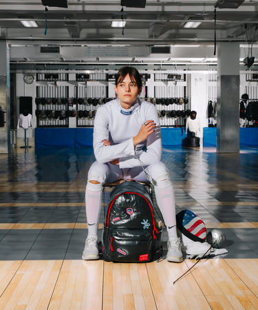 Person sitting on a black backpack in a gym setting