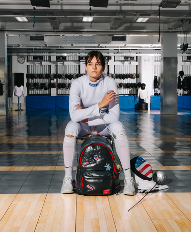 Person sitting on a black backpack in a gym setting
