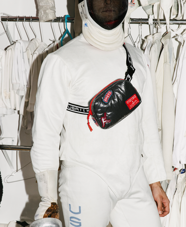 Person wearing a white outfit with a black and red bag in front of fencing whites