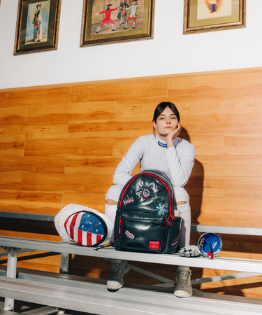 Person sitting on a bench with a backpack and framed pictures on the wall.