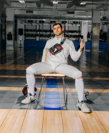 Person in fencing gear sitting on a chair in an indoor setting