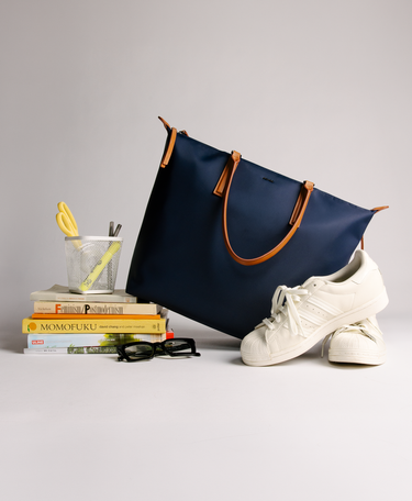 Studio Tote Navy on top of stack of books with sneakers 