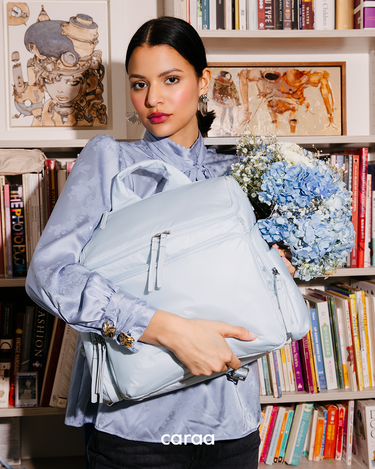 Woman holding Baby Bag in Baby Blue in front of bookshelf