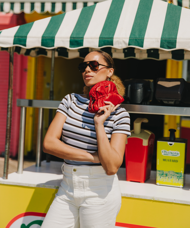 Woman holding a red pouch in front of a colorful food stand with striped awning.